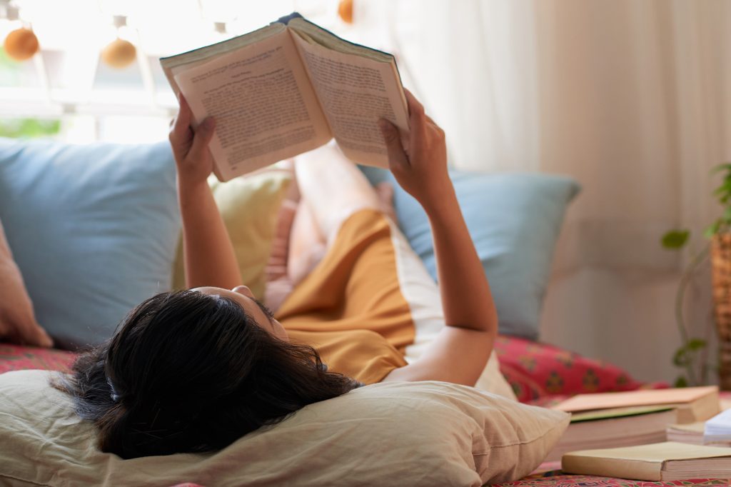 Mulher lendo um livro, deitada em uma cama.