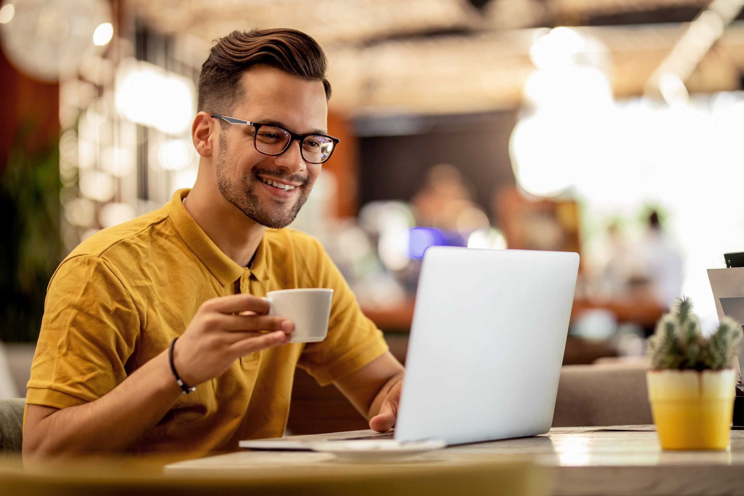 Homem sorrindo para computador enquanto toma café.